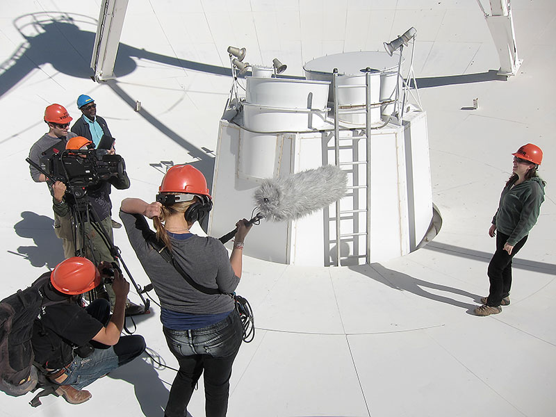 NRAO scientist Amy Reines (far right) enjoys a 'tour' of a VLA antenna hosted by VLA Operators Lead Gene Cole (far left, wearing blue helmet), as will thousands of visitors who will see the new film.